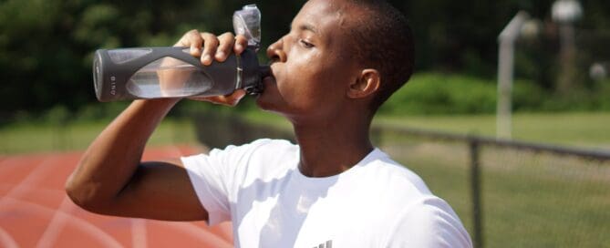 man standing on a running track drinking a refillable water bottle