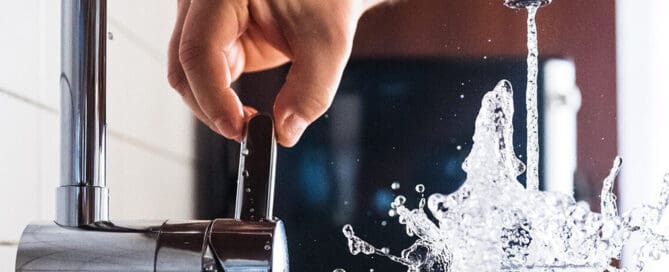 person turning on faucet filling cup with water