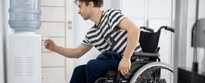 guy in wheelchair getting water from plastic jug water cooler