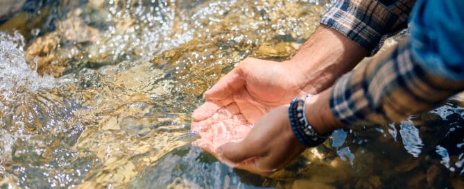 Native American man cupping water from river in his hands.